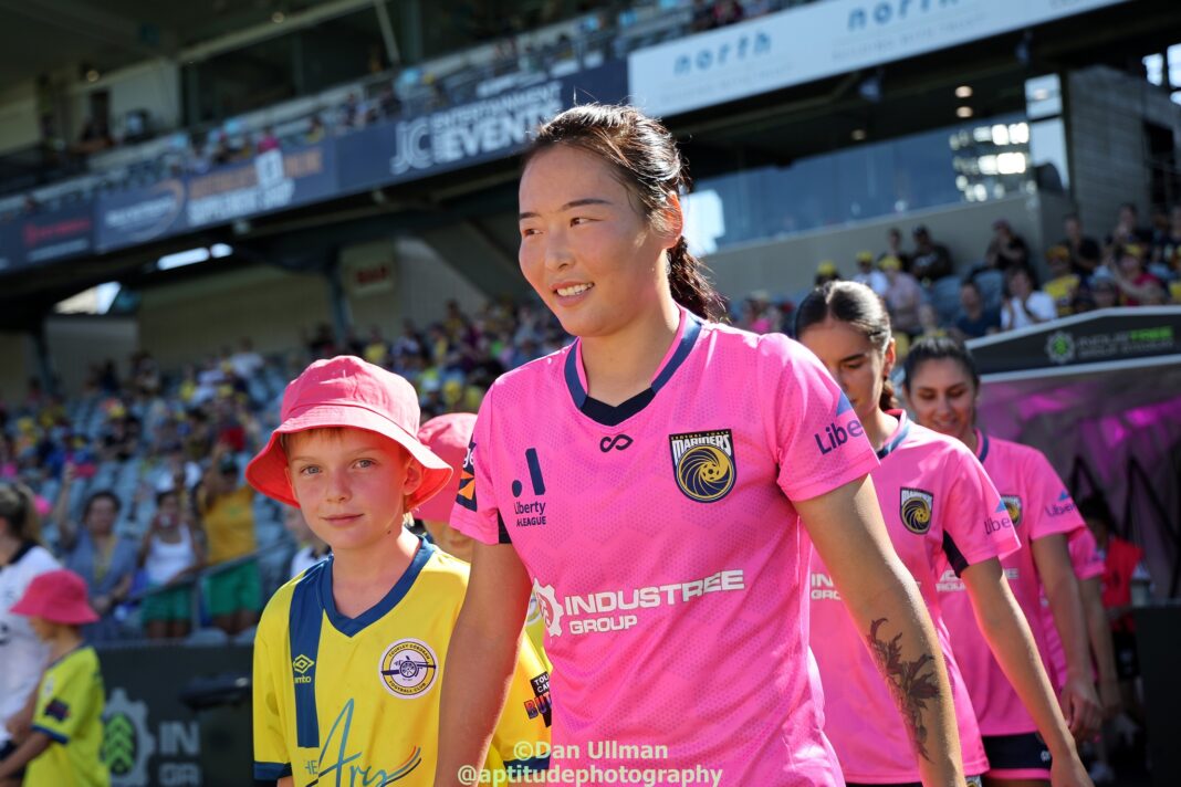 Central Coast Mariners forward Wurigumula walks out with a mascot, prior to the 2023-24 A-League Women game between the Mariners and Adelaide United at Central Coast Stadium. Photo credit: Dan Ullman (Instagram - @aptitudephotography )