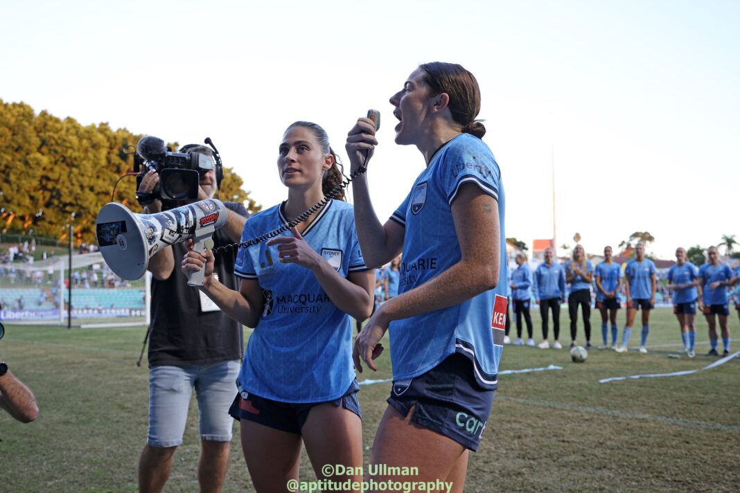 Tori Tumeth (assisted by Margaux Chauvet) leads The Cove’s post game chanting with The Cove’s megaphone, after Sydney FC defeated Central Coast Mariners in the 2023-24 A-League Women semi finals. The 2nd leg was played at Leichhardt Oval on April 27, 2024. Photo credit: Dan Ullman (Instagram - @aptitudephotography )