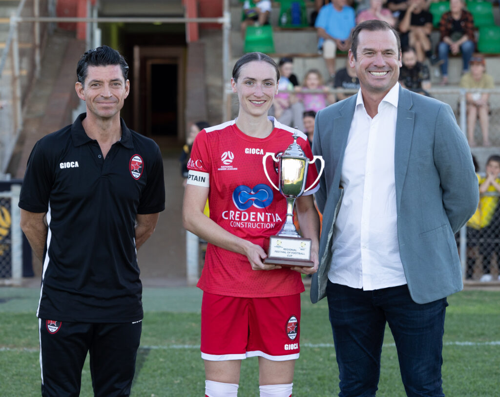 Perth RedStar captain Sarah Carroll (c) with the Regional Festival of Football Trophy, alongside RedStar Carlos Vega Mena (l) and Football West CEO Jamie Harnwell (r)